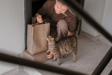 Contactless home delivery at the doorstep. A woman receives eco-packaged goods while her cat...