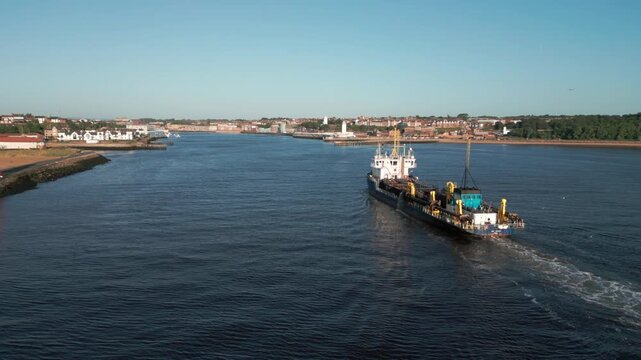Drone slowly follows dredging ship UKD Marlin up the River Tyne in South Shields on a sunny summer morning. Gulls can be seen at the rear of the ship