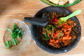Close-up of traditional Indonesian sambal made from chili and herbs in a stone mortar, garnished...