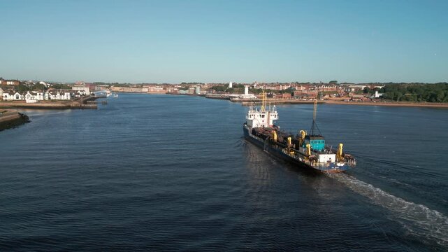 Drone flies away and tracks around dredging ship UKD Marlin on the River Tyne in South Shields on a sunny summer morning. Gulls can be seen at the rear of the ship