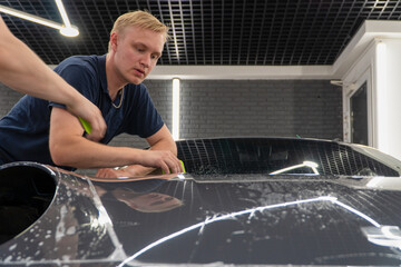 A car wrapping specialist applies a polyurethane film to the car. Detailer smoothes PPF. Car...