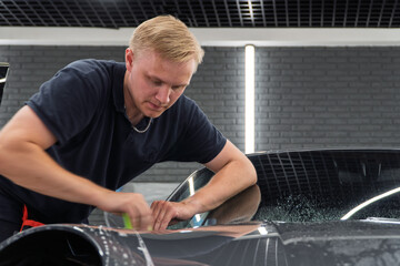 A car wrapping specialist applies a polyurethane film to the car. Detailer smoothes PPF. Car...
