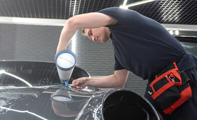 A car wrapping specialist applies a polyurethane film to the car. Detailer smoothes PPF. Car...