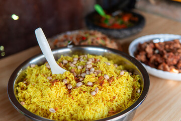 A traditional Indonesian meal featuring yellow rice topped with peanuts and fried shallots, served with assorted side dishes on a wooden table during a local gathering or celebration.