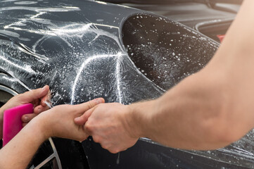 A car wrapping specialist applies a polyurethane film to the car. Detailer smoothes PPF. Car...