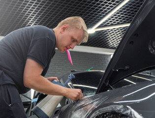 A car wrapping specialist applies a polyurethane film to the car. Detailer smoothes PPF. Car...
