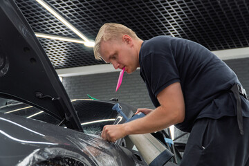 A car wrapping specialist applies a polyurethane film to the car. Detailer smoothes PPF. Car...