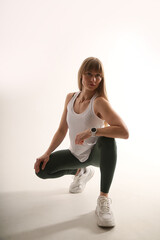 Sporty young woman in white top and dark leggings posing on white background, full length fitness...