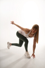 Fototapeta premium Sporty young woman in white top and dark leggings posing on white background, full length fitness studio shot, active lifestyle and workout concept.