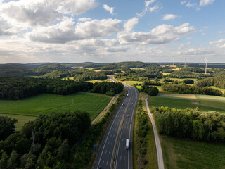 Aerial view of highway a9 crossing the Bavarian countryside near pegnitz, with trucks driving on asphalt road, green fields, forests and wind turbines in background
