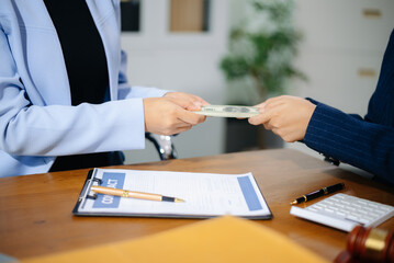 Two businesswomen in formal suits exchange cash over a contract document in an office. Bribery,...