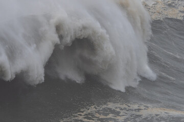Massive ocean wave crashing against rocky shoreline in Nazare, Portugal, legendary big wave surfing...
