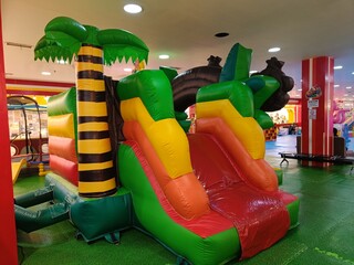 Inflatable bouncy castle with a slide, designed with a jungle theme, featuring a palm tree and...