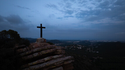 Large cross stands tall on rocky terrain. Casting a striking silhouette against the darkening sky....