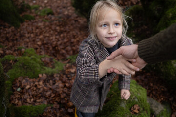 Little girl reaching for an adult's hand while navigating through a colorful autumn forest,...