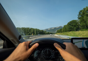 Gripping steering wheel while driving along winding mountain road, navigating GPS through scenic...