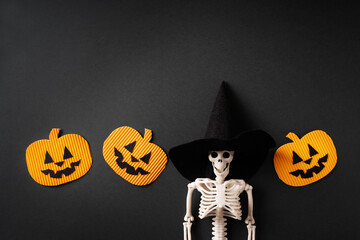 Skeleton in witch hat with pumpkins on black background