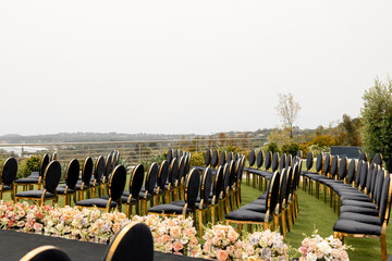 Rows of empty guest chairs at an outdoor wedding ceremony. Elegant black and gold velvet chairs...