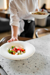 Waiter in white shirt serving fresh watermelon feta salad on a white plate in a modern dining area,...