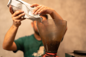 Man pouring coffee beans in a coffee grinder in cafe, prepares coffee in a cafe