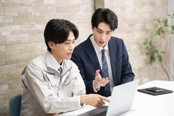 ゼネコンなどの現場で資料を確認する施工管理の作業服とスーツの男性　真剣に打ち合わせで確認する