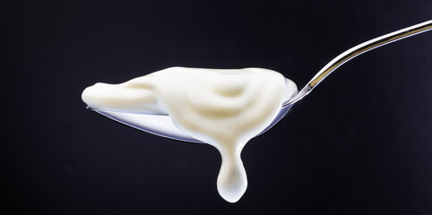 Loeffel mit Joghurt tropfend vor schwarzem Fond, Joghurt, Edelstahllöffel, 