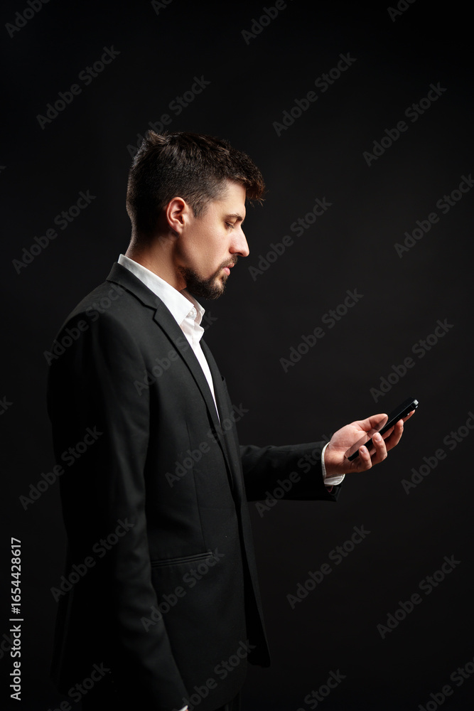 Aufkleber man in formal attire checks smartphone against a dark background during a professional setting