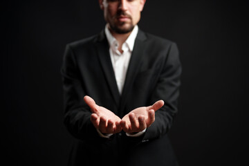 Businessman presenting hands forward in professional attire against a dark background while...