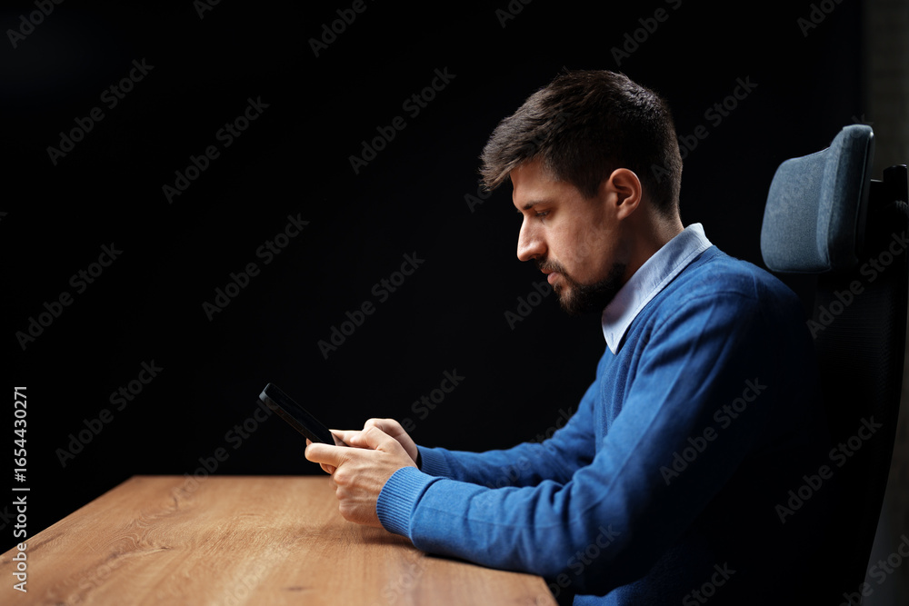 Aufkleber man using smartphone while sitting at a wooden desk in a dimly lit room during evening hours
