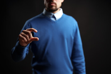 Person in blue sweater using hand gesture to symbolize measurement against dark background