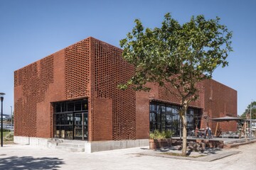 Modern brick building showcases innovative architecture in an urban park, featuring large windows and inviting outdoor seating areas, perfect for leisurely gatherings and events