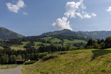 View of rolling green hills and forested slopes under a partly cloudy blue sky in Kitzbühel,...