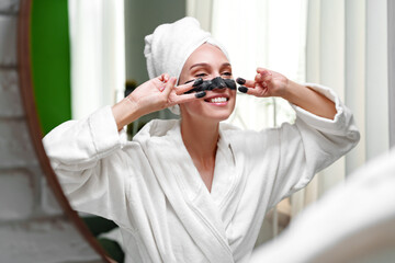 Woman enjoying a skincare routine while smiling in a bright, modern bathroom in the morning