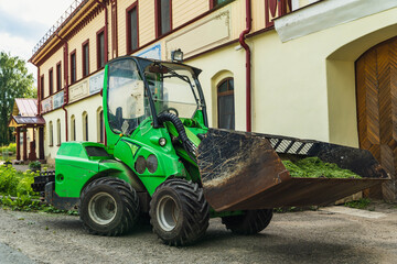 Skid steer loader removing grass cuttings in front of building