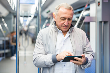Mature man with smartphone standing in subway car