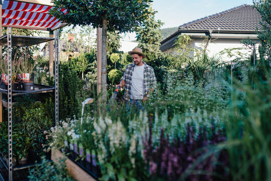 Garden center owner watering plants with hose in greenhouse.