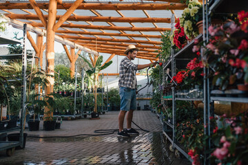 Garden center owner watering plants with hose in greenhouse.