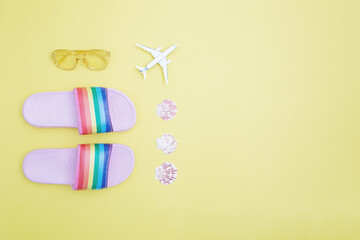 Rainbow slippers, toy airplane, seashells and sunglasses on a yellow background. Summer holiday, travel and vacation concept. Flat lay, copy space