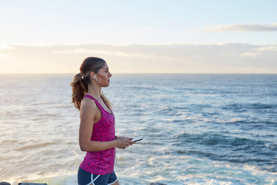 Fitness woman with phone at coastal headland on sunrise