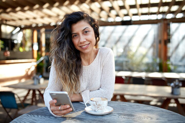 Young middle eastern woman enjoying time on phone at cafe