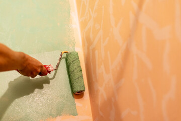 Hand of a person applying green paint with roller on wall, painting process in a home improvement...