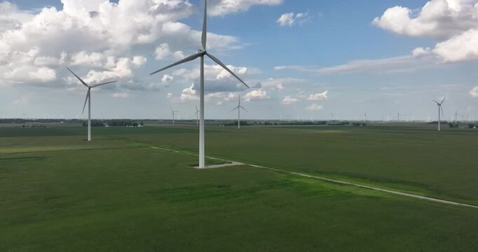 Aerial view of wind turbines standing tall amidst the vast green fields under a sky dotted with fluffy clouds, Monroeville, Indiana, United States.