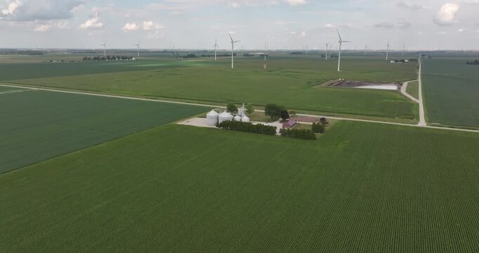 Aerial view of verdant fields, punctuated by towering wind turbines and clusters of silvery silos, blending rural charm with modern energy, Monroeville, Indiana, United States.