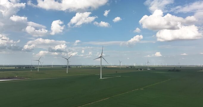 Aerial view of wind turbines rising from lush green fields under a partly cloudy sky, creating a scene of sustainable energy, Monroeville, Indiana, United States.