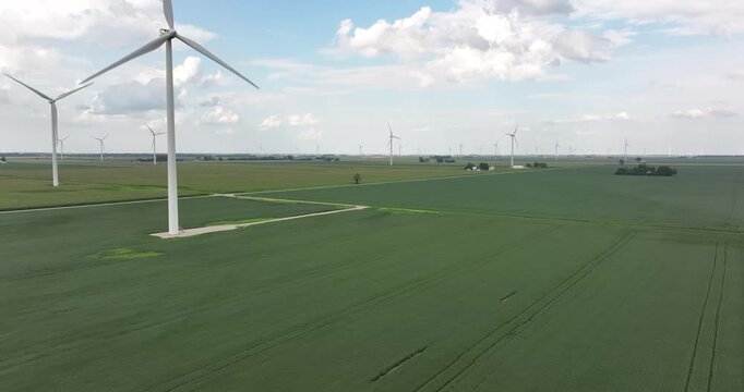 Aerial view of the wind turbines standing tall in vibrant green fields under a partly cloudy sky, Monroeville, Indiana, United States.