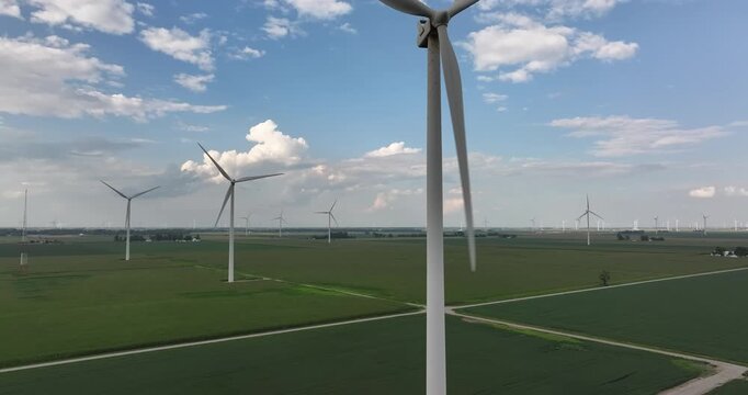 Aerial view of wind turbines standing tall in a vibrant green field under a partly cloudy sky, creating a striking contrast, Monroeville, Indiana, United States.