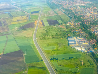 Aerial view of highway and green fields near city. Urban development, agricultural landscape, and...