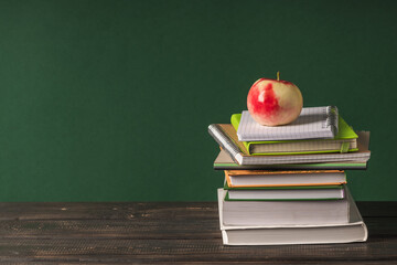 A stack of books and notebooks on a wooden table on a green background. Back to school concept.