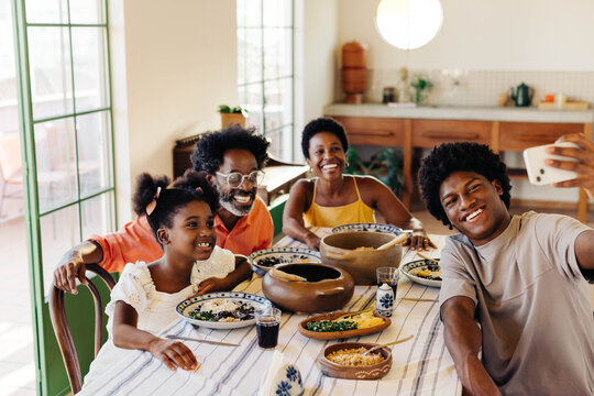 Brazilian family taking a selfie at the dining table, serving traditional food - Powered by Adobe