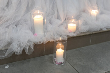 Flickering candles illuminate a wedding venue adorned with flowing white fabric. Soft petals...